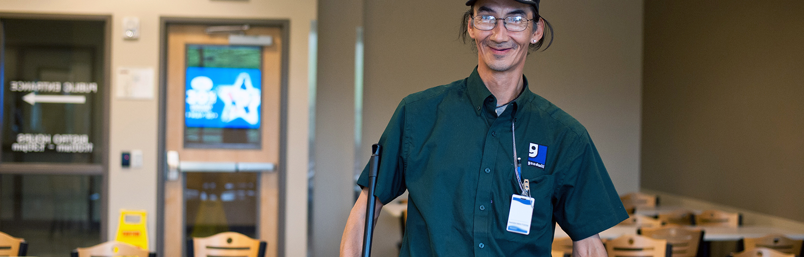 Man smiles holding broom in room he is cleaning